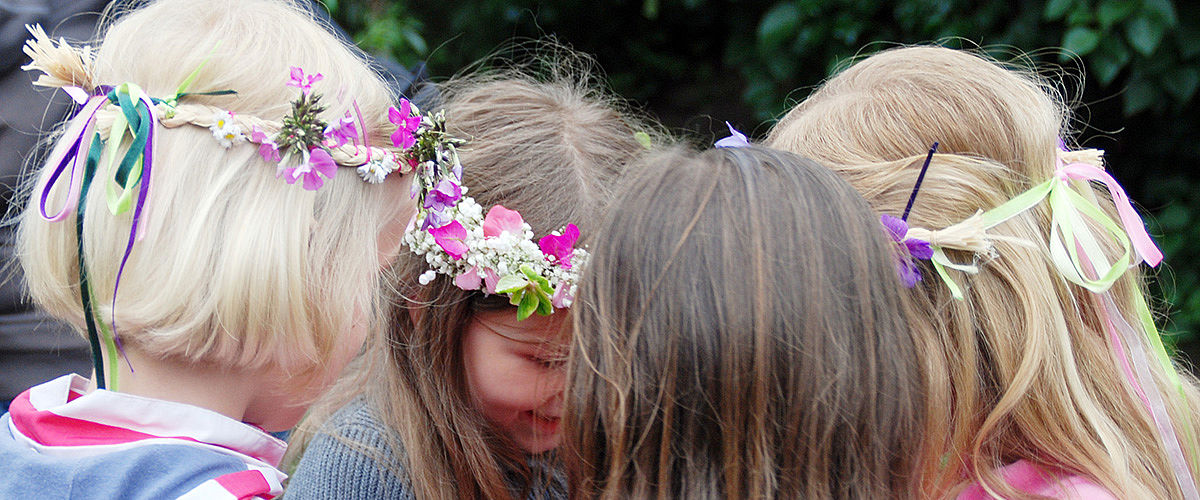 Vier Mädchen stehend im Kreis mit Blumenlränzen im Haar
