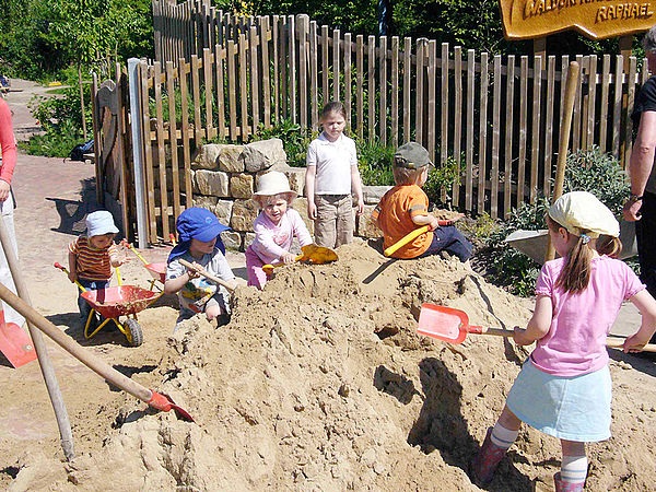 Viele Kinder spielen auf einem Sandhaufen mit Schafueln und Sandspielzeug