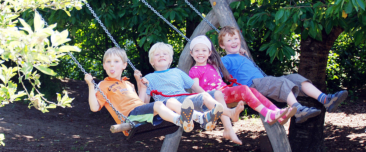 Vier Kinder lachend auf einer Schaukel im Garten des Kindergartens