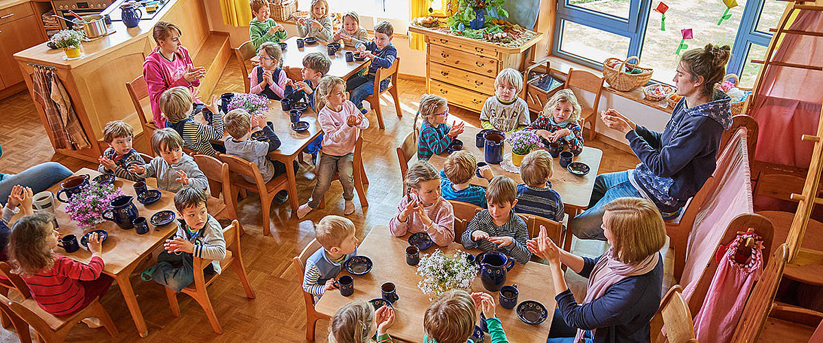 Große Kindergartengruppe vor dem Essen an gedeckten Tischen